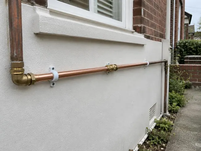Repaired copper water pipe fixed along an exterior house wall beside a window in Randwick