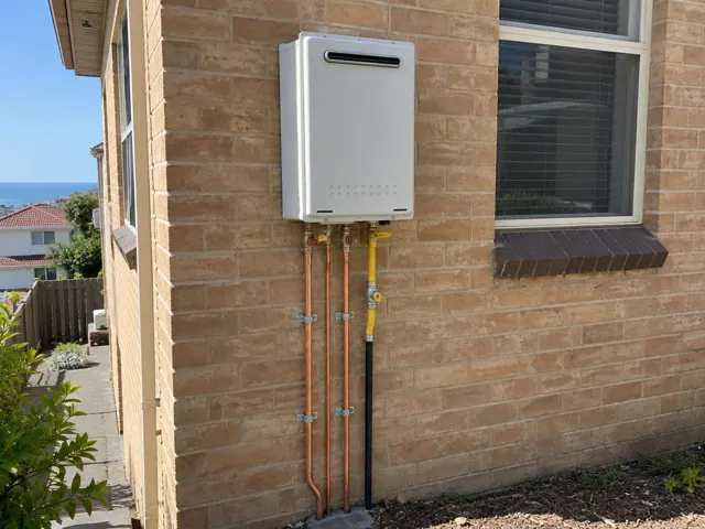 Wall-mounted hot water unit on a brick exterior wall with copper and gas pipes in Coogee